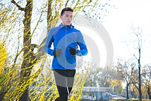 Young Sports Man Running in the Park in Cold Sunny Autumn Morning. Healthy Lifestyle and Sport Concept.