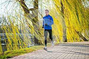 Young Sports Man Running in the Park in Cold Sunny Autumn Morning. Healthy Lifestyle and Sport Concept.