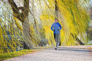 Young Sports Man Running in the Park in Cold Sunny Autumn Morning. Healthy Lifestyle and Sport Concept.