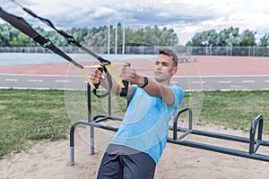 Young sports man summer city, pulls up and wring out on his hinges, straps horizontal bar, healthy lifestyle fitness