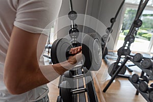 Young sports man in a white trendy T-shirt picks up a dumbbell. Guy is training in the gym. Close-up of a man`s hand with dumbbel