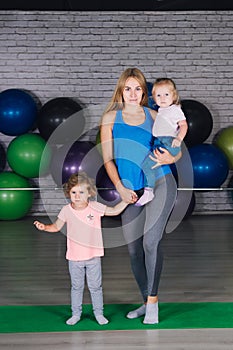 Young sports mom and baby girls do exercises together in the gym