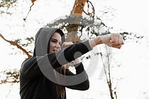 Young sports woman boxing in the park. Young woman is training a direct hit, focus on eyes