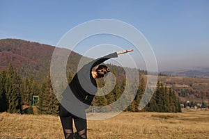 Young sports woman doing yoga exercise on the mountains and sky background in the autumn