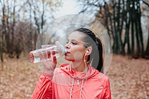 Young sports woman drinking fresh water from the bottle in the autumn park . Sport lifestyle.