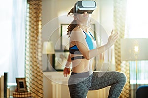 Young sports woman in modern living room in VR glasses workout