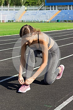 Young sportsgirl tying her shoelaces on run track in stadium sport and fitness concept