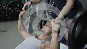 Young sportsman is doing his effort in inclined bench presses with his trainer on the gym.