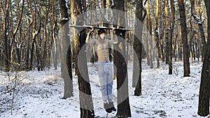 Young sportsman doing static exercises on horizontal bar at forest. Athletic man working out at winter nature. Sportive