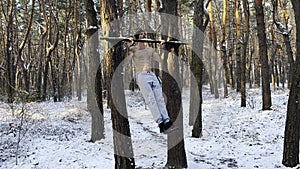 Young sportsman doing static exercises on horizontal bar at forest. Athletic man working out at winter nature. Sportive