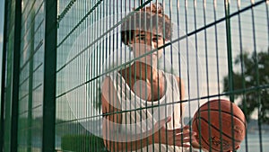 Young sportsman posing basketball court portrait. Curly bad guy looking camera