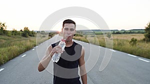 Young sportsman walking to camera, looking into it, drinking a bottle of water