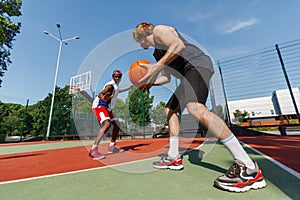 Young sportsmen playing basketball at outdoor court on sunny summer day