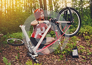 Young sportswoman bicyclist repairing her mtb bike in the forest