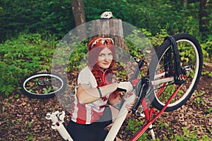 Young sportswoman bicyclist repairing her mtb bike in the forest