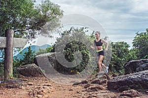 Young sportswoman cross country running on dirty rocky footpath in mountains in summer. Fit girl jogging outdoors in