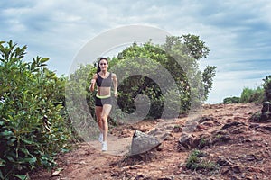 Young sportswoman cross country running on dirty rocky footpath in mountains in summer. Fit girl jogging outdoors in