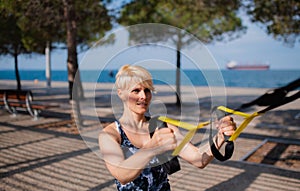 A young sportswoman doing exercise with TRX fitness straps outdoors.