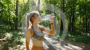 Young sportswoman drinking water after run at sunset in summer forest