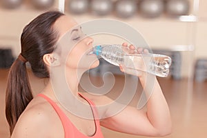 Young sportswoman drinking water after training