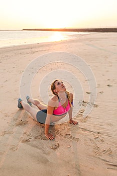 young sportswoman in earphones with smartphone in armband case doing exercise on sandy