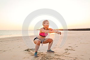 young sportswoman in earphones with smartphone in armband case doing squat