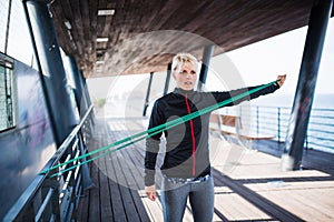 A young sportswoman with elastic band doing exercise outdoors in city.