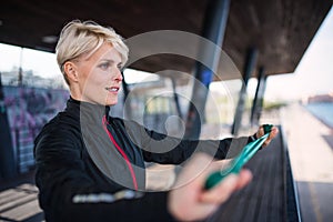 A young sportswoman with elastic band doing exercise outdoors in city.