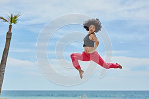 Young sportswoman jumping on beach with hands on waist