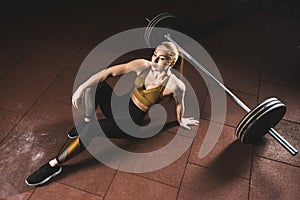 Young sportswoman resting on floor near barbell