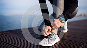 A young sportswoman with smartwatch outdoors on beach, tying shoelaces.