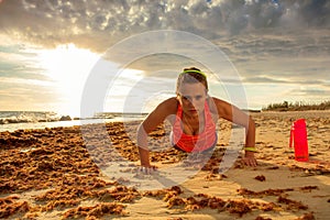 Young sportswoman in sport clothes on seashore doing pushups