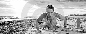 Young sportswoman in sport clothes on seashore doing pushups