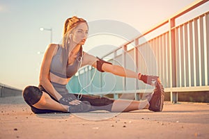 Young sportswoman stretching and touching her toes with her hand outdoors. Sporty girl stretching on the bridge.