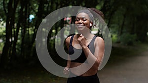 Young sporty african american lady athlete enjoying morning run workout in public park, listening to music via earbuds