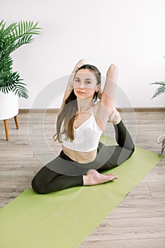 Young sporty attractive Caucasian woman in sports pants and top, practicing yoga, doing Mermaid exercise, Eka Pada
