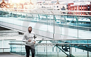 Young sporty black man runner running on the bridge outside in a city.