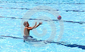 Young sporty boy playing ball in big outdoor swimming-pool