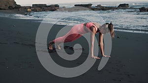 Young sporty Caucasian woman doing legs exercises on wet sandy beach.