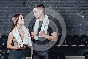 Young sporty couple guy and girl standing in gym. During this, the white scumbag is held on the neck.