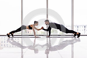 Young sporty couple working out together in a gym doing plank exercises while holding each other for one hand