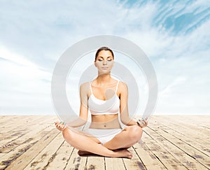 Sporty, young and beautiful woman in swimsuit meditating on a pier at summer. Sport and yoga concept.