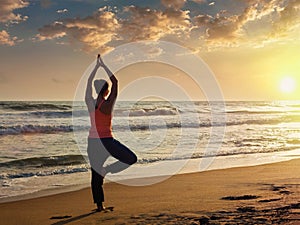 Young sporty fit woman doing yoga tree asana on beach
