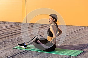 Young sporty girl in black sportwear sitting on mat and have a strong hurt problem with back, spasm painful. Gripping spinal with