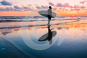 Young and sporty girl go to surfing. Beautiful woman in wetsuit and sunset on ocean