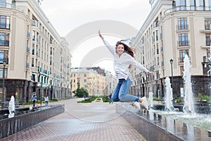 Young sporty girl jumping for joy at the fountain in the residential complex. Female in flight with his hands up