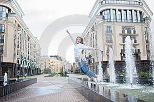 Young sporty girl jumping for joy at the fountain in the residential complex. Female in flight with his hands up