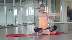 Young sporty girl in sports clothes doing warm-up on the rug in the gym with tape