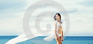 Young, sporty and happy woman posing with a blowing silk on a beach