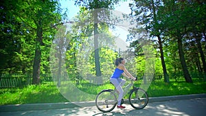 Young sporty happy woman rides a bike through summer park. Girl on bike outside. summer time. sunny day. sun glares.